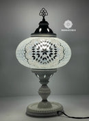 Lámpara turca de mesa encendida, reflejando tonos cálidos a través del mosaico espejado artesanal.